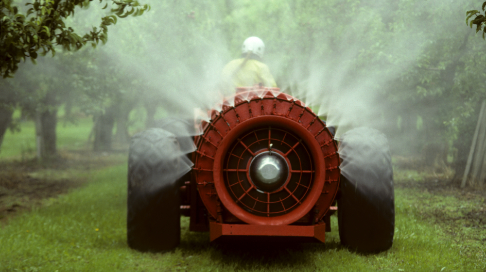 A pesticide sprayer rolls through an apple orchard.